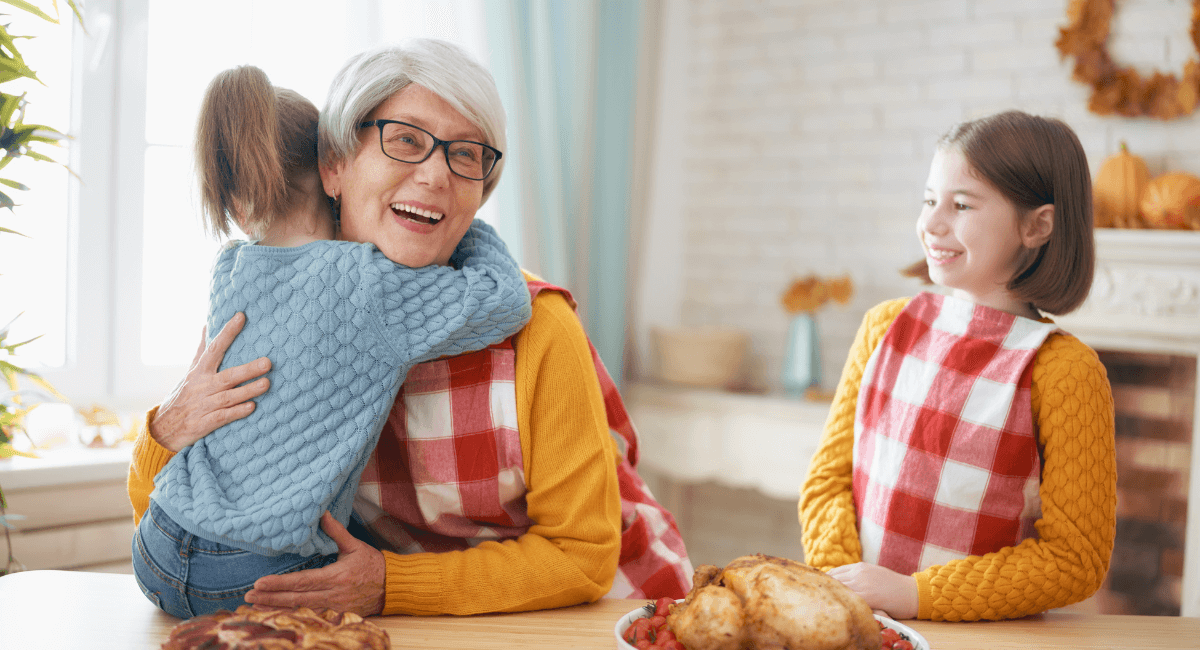 Woman hugging one young child while another looks on and smiles